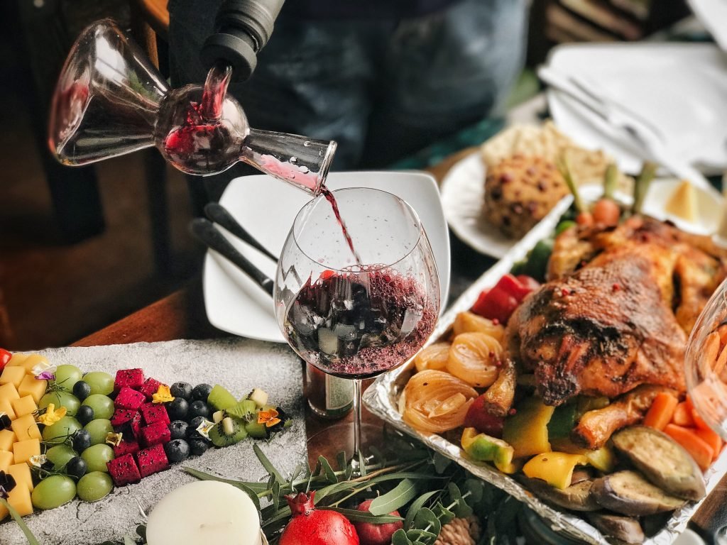 A vibrant brunch table featuring a decanter pouring Tribu Malbec red wine into a glass, alongside a sumptuous platter of roasted chicken and fresh fruit.