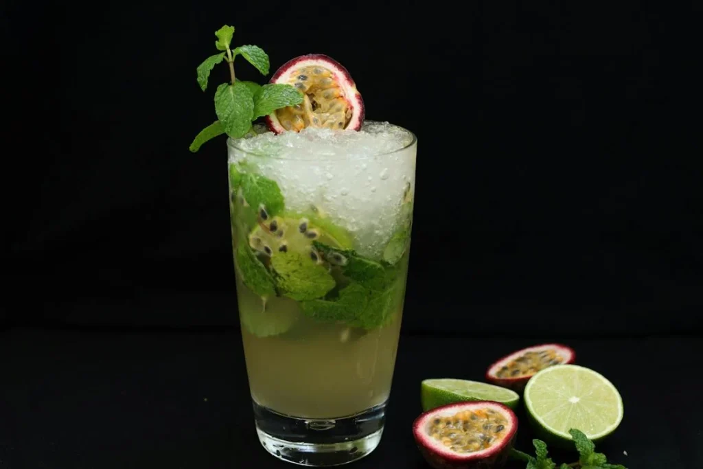 A chilled highball glass filled with a passion fruit cocktail, garnished with fresh mint and a slice of passion fruit, set against a dark background with vibrant lime accents.