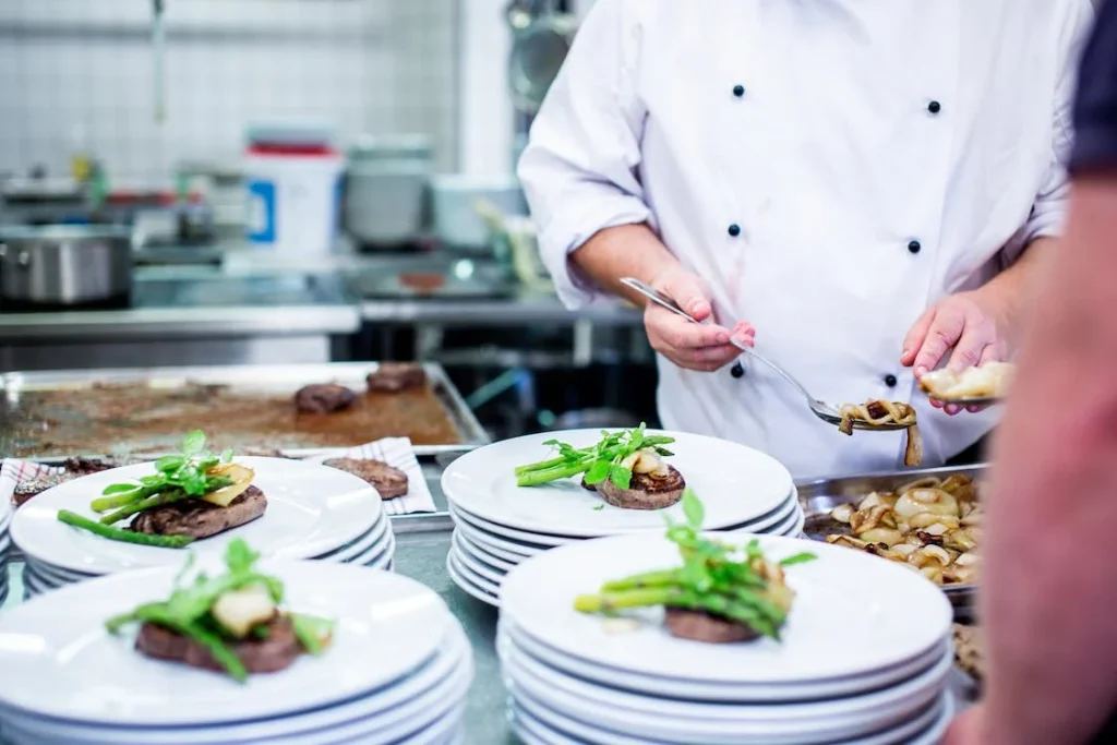 Busy kitchen scene capturing a chef's precise garnishing of plated steaks with fresh greens, exemplifying the meticulous preparation behind chef-recommended dishes.