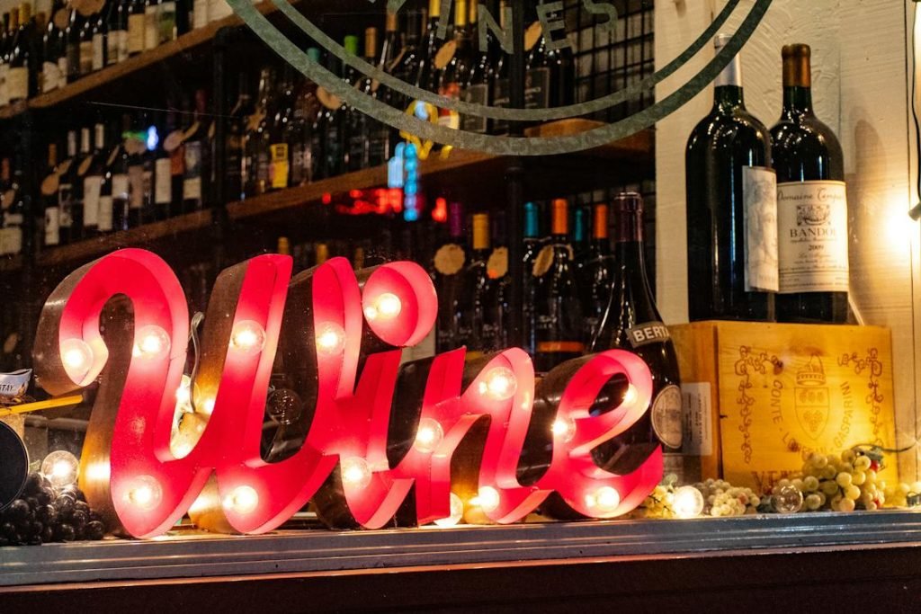 Vibrant neon 'Wine' sign illuminating a curated collection of fine wines in a cozy downtown wine bar setting.