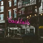 A neon sign spelling 'Cocktails' illuminates the front of a trendy downtown bar, inviting patrons to explore its menu of inventive drinks.