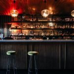 Elegant bar setting in Yaletown, Vancouver, showcasing an array of spirits under warm lighting, with plush bar stools inviting an intimate dining experience.
